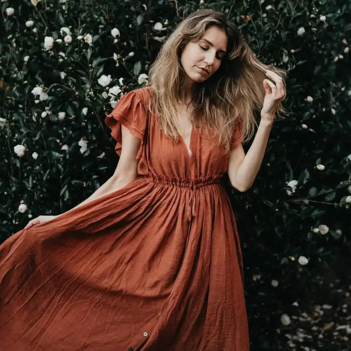 Une robe en lin de couleur rouille fluide avec un décolleté en V et des manches courtes à volants.